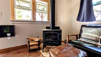 Ein gemütliches Wohnzimmer mit Kaminofen, Fenster mit Aussicht, einer Ledersofa und einem Holzstuhl.