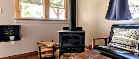 A cozy living room with a wood-burning stove, a window with a view, a leather sofa, and a wooden chair.