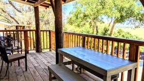 Um deck de madeira com uma mesa de piquenique e cadeiras, rodeado por árvores.