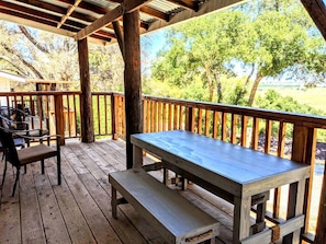 Una terraza de madera con una mesa de picnic y sillas, rodeada de árboles.