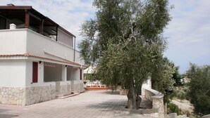 A modern two-story house with a stone facade, a balcony, and a large tree in the foreground. - Vacation house located in quiet hillside area with sea view and swimming pool (Vieste)
