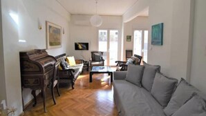 Una sala de estar con un piano, sofá, sillones, suelo de madera y televisor.