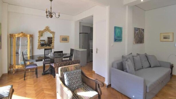 Una sala de estar con un sofá, una mesa de comedor con sillas, un espejo y una araña.