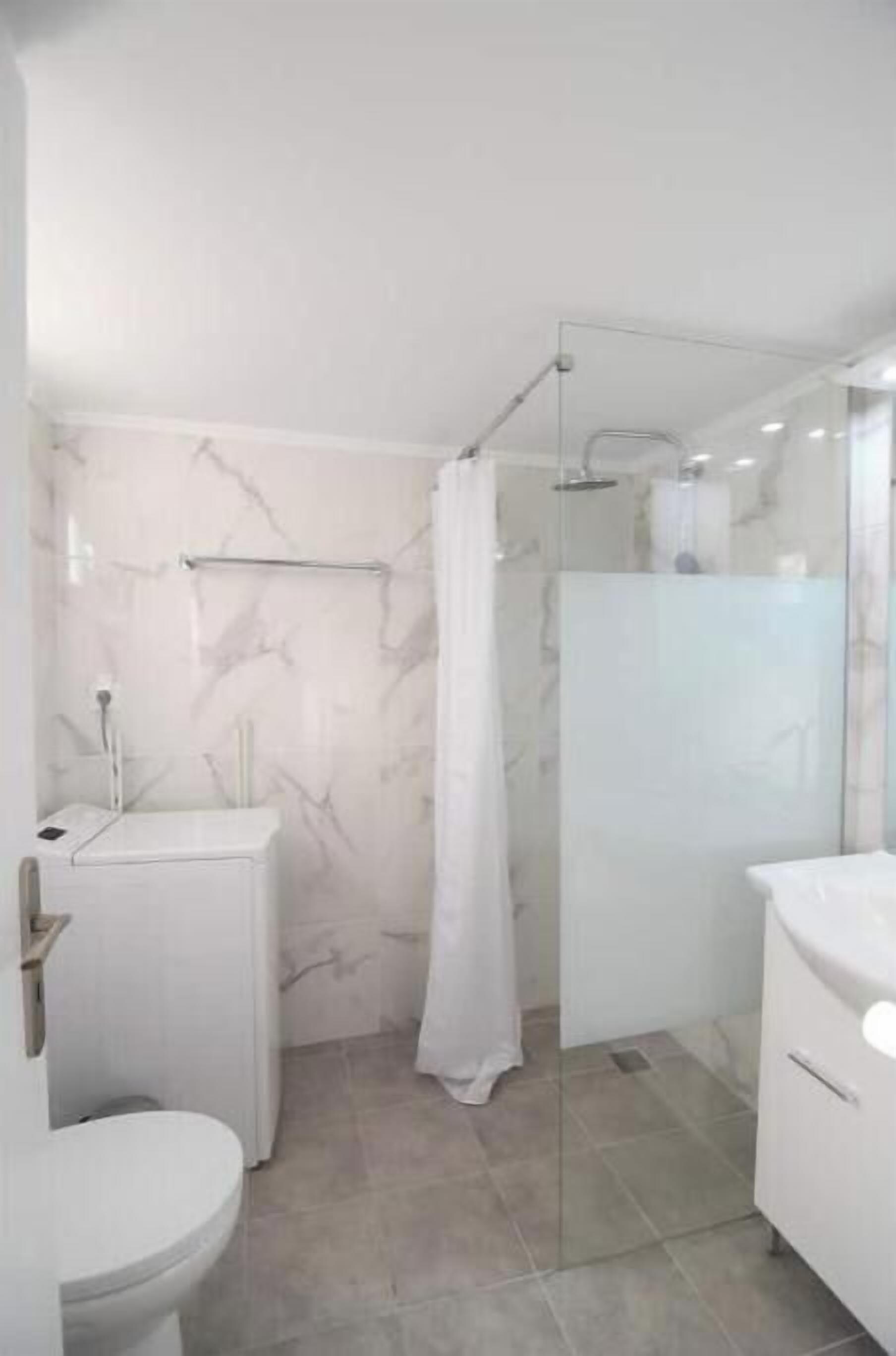 Een badkamer met toilet, wastafel, douche met glazen deur en een marmeren wand.