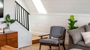 A loft-style living room with a high ceiling, wooden beams, a staircase, and a skylight.