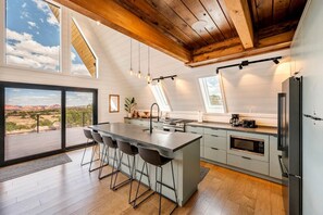 A modern kitchen with a large island, bar stools, a dining area with a view, and a high ceiling with exposed beams. - Secluded A-frame with Stunning Desert Views in Torrey, Utah (Torrey)