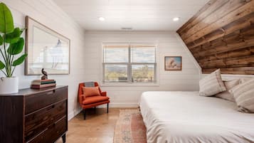 A bedroom with a wooden ceiling, a bed, a dresser, a chair, a window with blinds, and a plant.