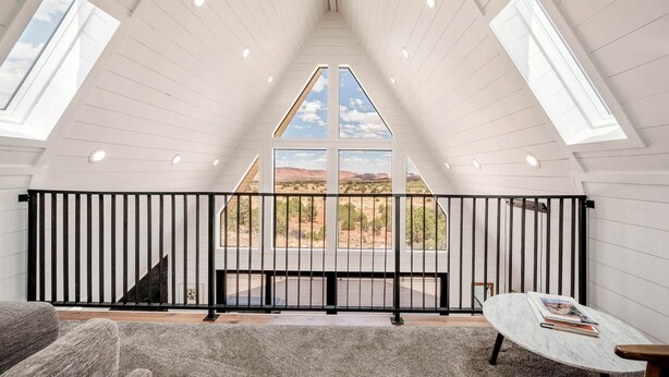 A spacious room with a high ceiling, skylights, a black railing, a view of the desert, and a small table with a book.