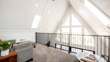 A spacious loft with a high ceiling, a black railing, and a view of the outdoors.
