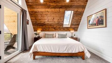 A bedroom with a wooden ceiling, a skylight, a bed with white bedding, two bedside tables with lamps, and a framed picture on the wall.