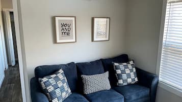 A dark blue sofa with patterned cushions, a framed quote on the wall, and a window with blinds.