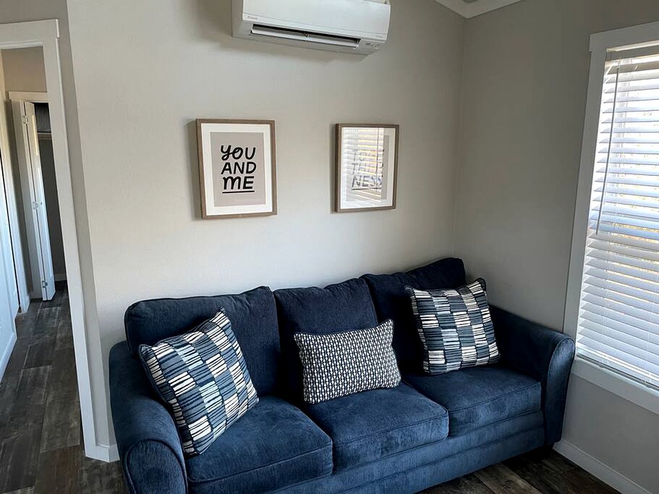 A dark blue sofa with patterned cushions, a framed quote on the wall, and a window with blinds.