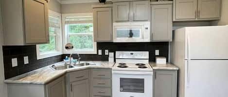 A kitchen with white cabinets, a microwave, stove, and refrigerator.
