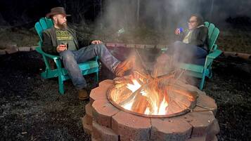 Two people sitting on green Adirondack chairs around a fire pit with a brick fire ring.