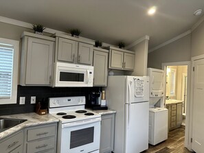 A kitchen with white cabinets, a microwave, stove, refrigerator, and a washing machine.