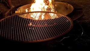 A grill with flames, a metal grate, and a partial view of a person. - Luxurious Safari Tent, Amazing for Glamping Vacations near Seguin, Texas (Seguin)