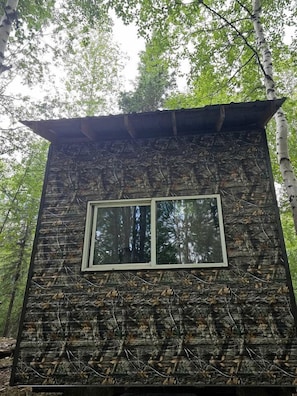 Una cabaña rústica con una ventana, rodeada de árboles.