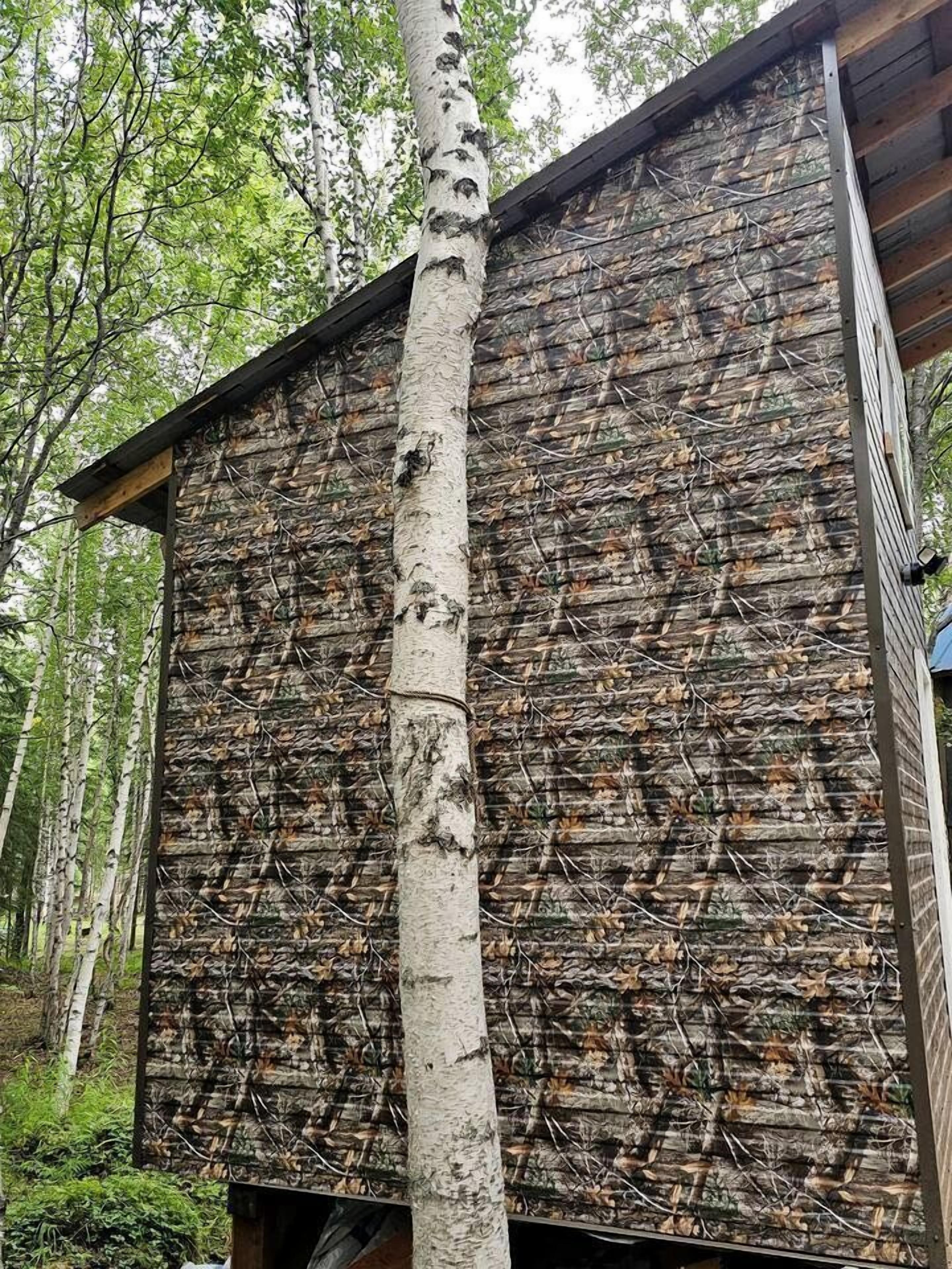 A wooden cabin with a camouflage exterior, surrounded by trees.