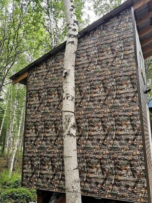 Puinen mökki, jonka ulkopinta on naamioitu, ja jonka ympärillä on puita.