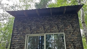 A rustic cabin with a window, surrounded by trees. - Peaceful Cozy Cabin Stay With Play Area Close To River For Fishing And Easy Outdoor Fun in Houston, Alaska (Houston)
