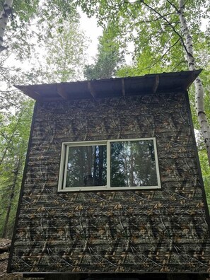 A rustic cabin with a window, surrounded by trees. - Peaceful Cozy Cabin Stay With Play Area Close To River For Fishing And Easy Outdoor Fun in Houston, Alaska (Houston)