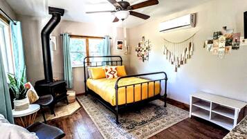 A bedroom with a bed, a ceiling fan, a heater, a window, and a wall-mounted air conditioner.
