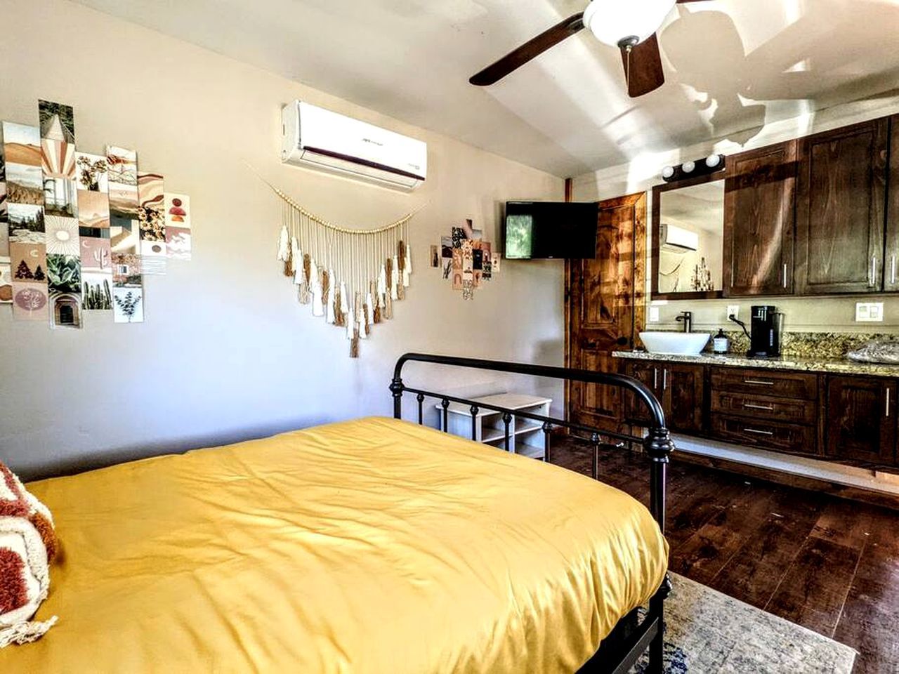 Ein Schlafzimmer mit Bett, Schreibtisch, Stuhl, Klimaanlage, Fernseher und einem Badezimmer inklusive Waschbecken und Spiegel.