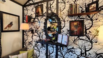 A room with a tree-themed wallpaper, a mirror, framed pictures, and bookshelves.