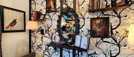 Una habitación con papel tapiz con motivos de árboles, un espejo, cuadros enmarcados y estanterías.