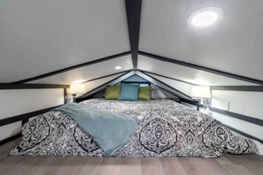 Een slaapkamer met een schuine plafond, een bed met gestreepte beddengoed, twee bedlampen en een raam.