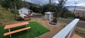 Une maison avec un porche à l’avant, un petit abri de jardin, un foyer et une table de pique-nique.