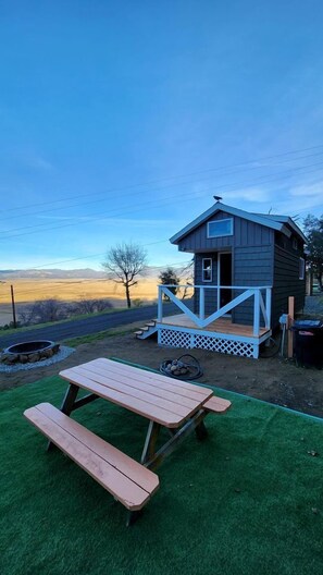 Une petite cabane avec une terrasse en bois et une table de pique-nique, située dans un cadre rural.
