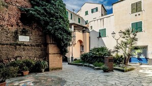 A courtyard with cobblestone flooring, a brick wall with greenery, and traditional buildings with shutters.