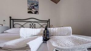 A neatly made bed with white linens, a bottle of shampoo, and a painting on the wall.