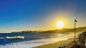 A beach with waves, a sunset, and a flag.
