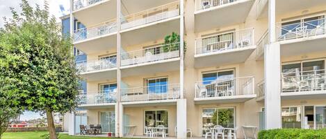 Un edificio de varios pisos con balcones, mobiliario exterior y un césped bien cuidado.
