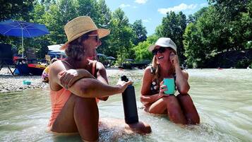 Two people in a river, one holding a water bottle, and another holding a mug.