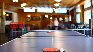 Ett bordtennisbord med ett racket och en boll i ett rum med träpanel i taket och träbord.