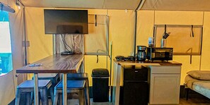 Une cuisine compacte équipée d’un réfrigérateur, d’un four à micro-ondes et d’une cuisinière, d’une petite table avec des chaises et d’un téléviseur fixé au mur.