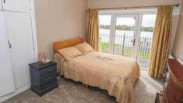 A bedroom with a bed, a dresser, a nightstand, and a view of a body of water through a sliding glass door.