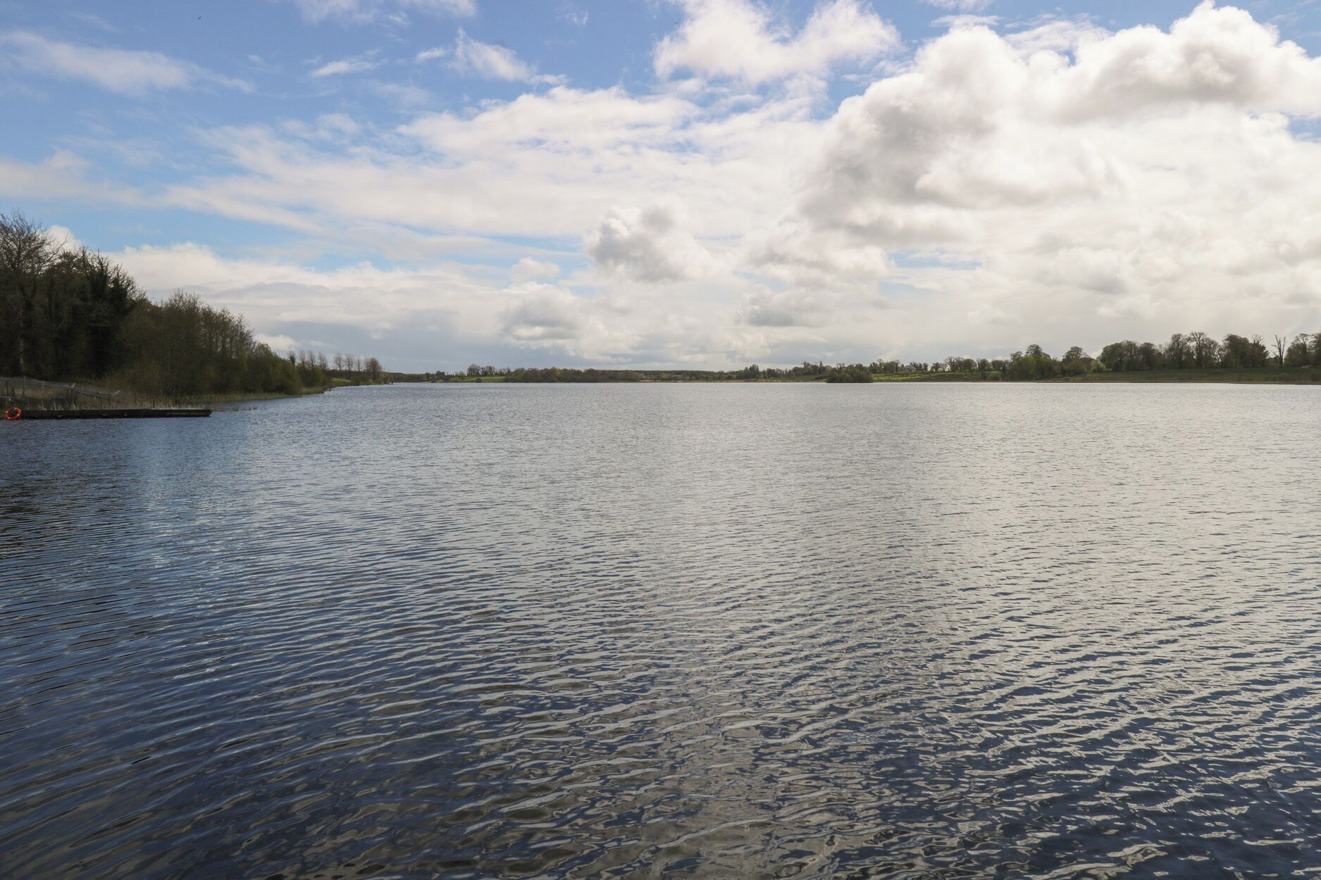 A calm lake with a wooden dock on the left and a forested shoreline.