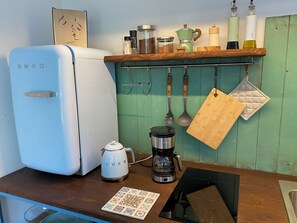 Una cocina con un refrigerador blanco antiguo, una cafetera, un hervidor y utensilios de cocina colgantes.