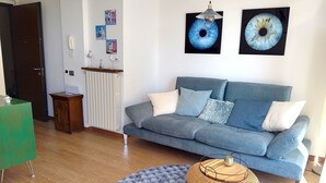 A living room with a blue sofa, a round wicker table, a fluffy rug, and wall art. - Lake view & tranquillity, Villa Laguna Blue, whirlpool & sauna-10 minutes walk to the lake (Gardone Riviera)