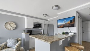 Una cocina moderna con microondas integrado, refrigerador y isla de encimera de granito con taburetes de bar.