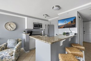 Eine moderne Küche mit integriertem Geschirrspüler, Kühlschrank und einer Kücheninsel mit Granitplatte und Barhocker.