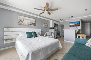 Ein modernes Hotelzimmer mit einem großen Bett, einem Deckenventilator, einem Fernseher, einer Küchenzeile und einer kleinen Sitzecke.