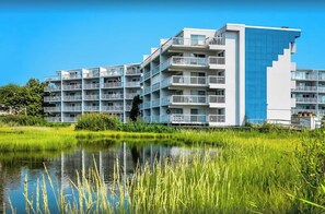 Ein modernes Mehrstöckhotel mit Balkonen, einem sich spiegelnden Wasserspiegel davor und üppiger Bepflanzung.