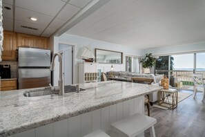 Eine moderne Küche mit einem Edelstahlkühlschrank, einer Granitarbeitsplatte und einem großen Fenster mit Blick auf einen Balkon.
