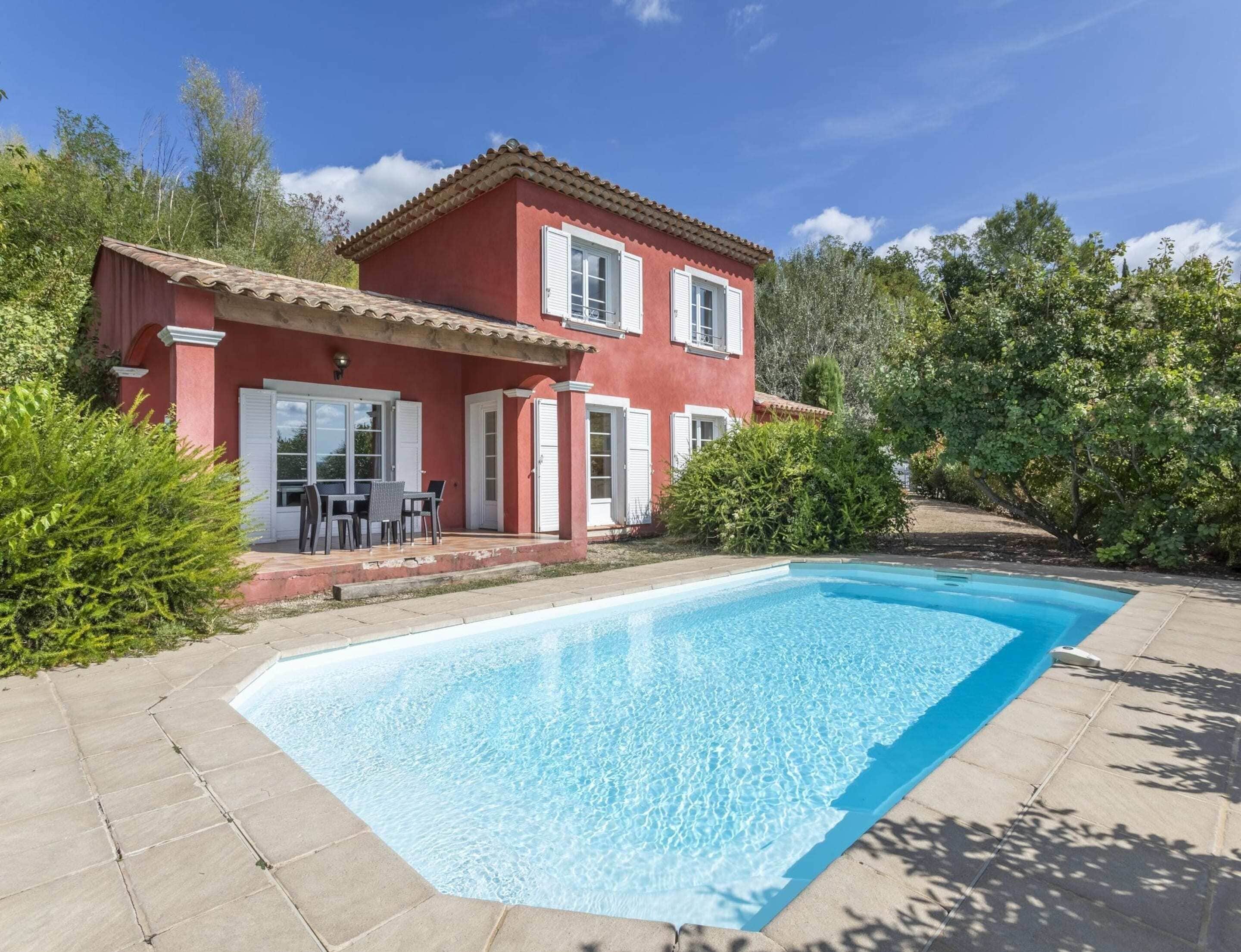 Une maison à deux étages avec une piscine, entourée de verdure.