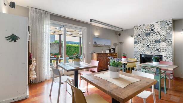 A dining area with a wooden table, chairs, and a kitchen area with a patterned backsplash. - Melloni Street Home - Lavender Room (Dolo)